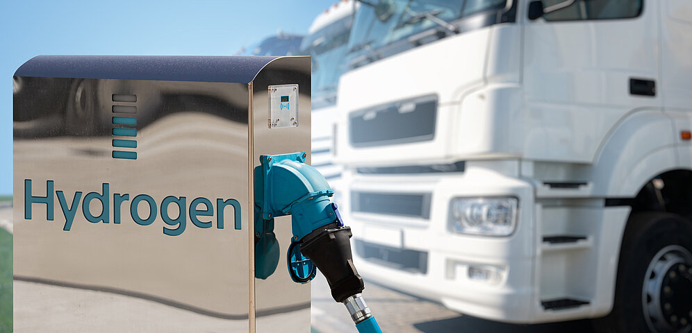 Wasserstoff-Zapfsäule mit der Aufschrift Hydrogen und dahinter parkende LKWs