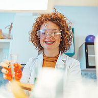 Person in a lab coat holding a small container with liquid in a laboratory setting.
