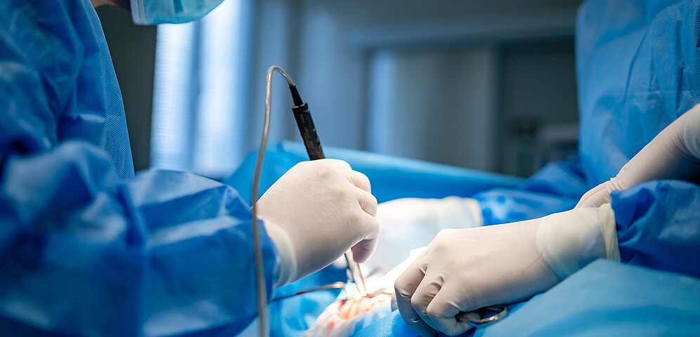 Picture of an operation on a patient with one doctor holding a medical instrument and one holding a suction instrument.
