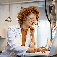 Zwei Frauen in einem Labor tragen Schutzkleidung und betrachten eine Petrischale.