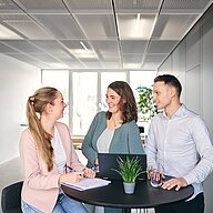 Three KNF employees standing at a table at KNF Neuberger GmbH in Freiburg-Munzingen and having a meeting. 
