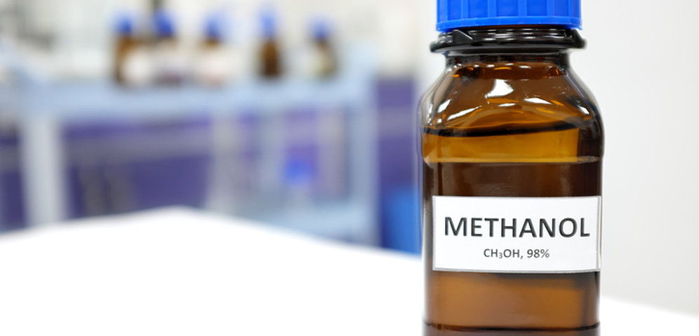 Braune Glasflasche mit Aufschrift Methanol CH3OH, 98% steht auf dem Tisch eines Labores