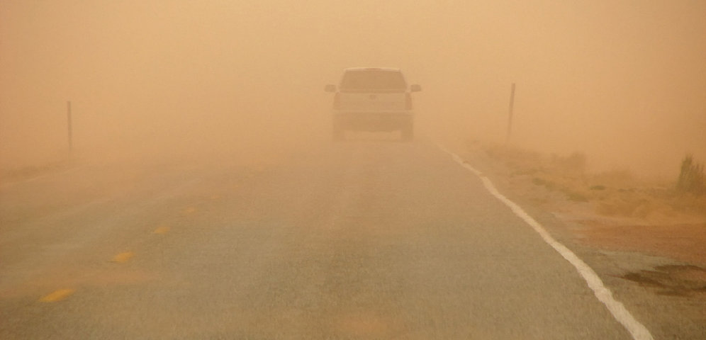 A white car drives along a road in thick Saharan dust