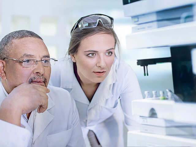 Two employees of a laboratory observe the function of a laboratory device 