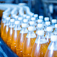 Rows of plastic bottles filled with orange liquid on an automated production line.