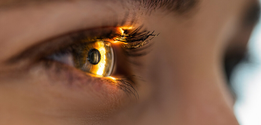 Nahaufnahme eines Auges, auf das Licht scheint, und zwar wahrscheinlich im Rahmen einer medizinischen Anwendung wie einer Kataraktoperation.